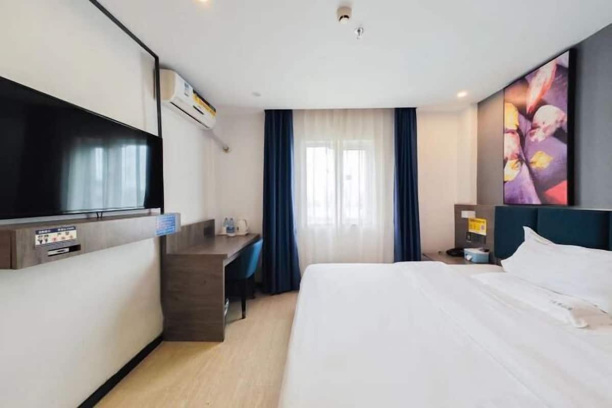 A hotel room with a bed, desk, TV, and a painting on the wall.