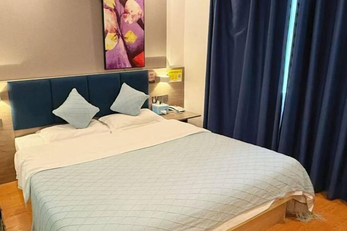 A hotel room with a bed, a nightstand, a lamp, and a painting on the wall.
