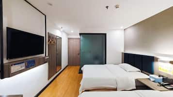 A hotel room with two beds, a TV, a desk with a computer, and a wardrobe.