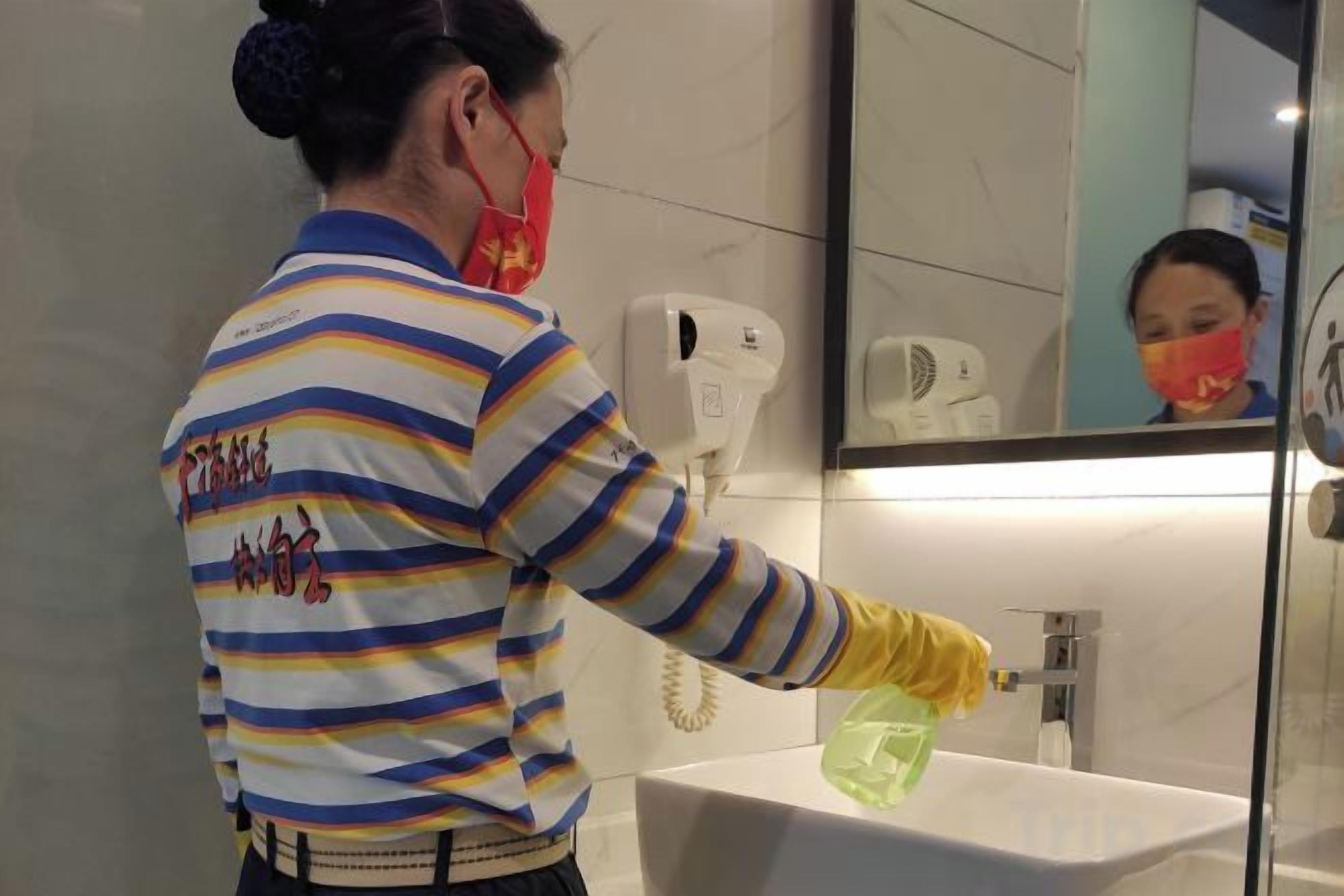 A person cleaning a sink in a bathroom with a mirror above it.