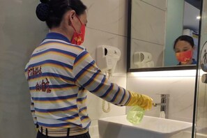 Una persona limpiando un lavamanos en un baño con un espejo encima.