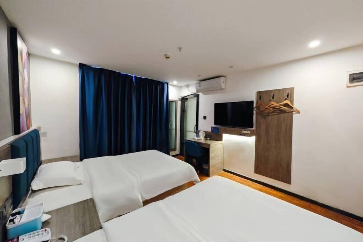 A hotel room with two beds, a desk, a TV, and a coat rack.