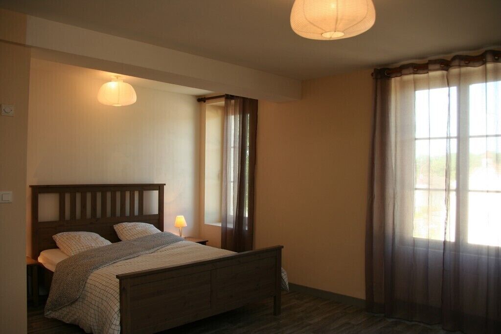 Un dormitorio con una cama de madera, una lámpara de noche y un ventanal con cortinas.