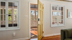 A room with two white-framed windows, a wooden door, and a green couch. - Elevated Potomac River Retreat - King Suite - Riverfront - Large Screened Porch (Sharpsburg)