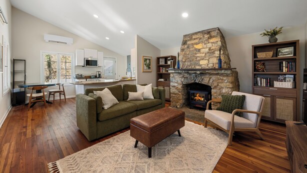 A spacious living room with a stone fireplace, a green sofa, a wooden coffee table, and a bookshelf. - Elevated Potomac River Retreat - King Suite - Riverfront - Large Screened Porch (Sharpsburg)