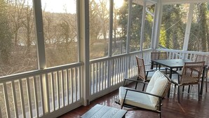 A covered patio with wicker furniture and a table, large windows, and a view of trees. - Elevated Potomac River Retreat - King Suite - Riverfront - Large Screened Porch (Sharpsburg)