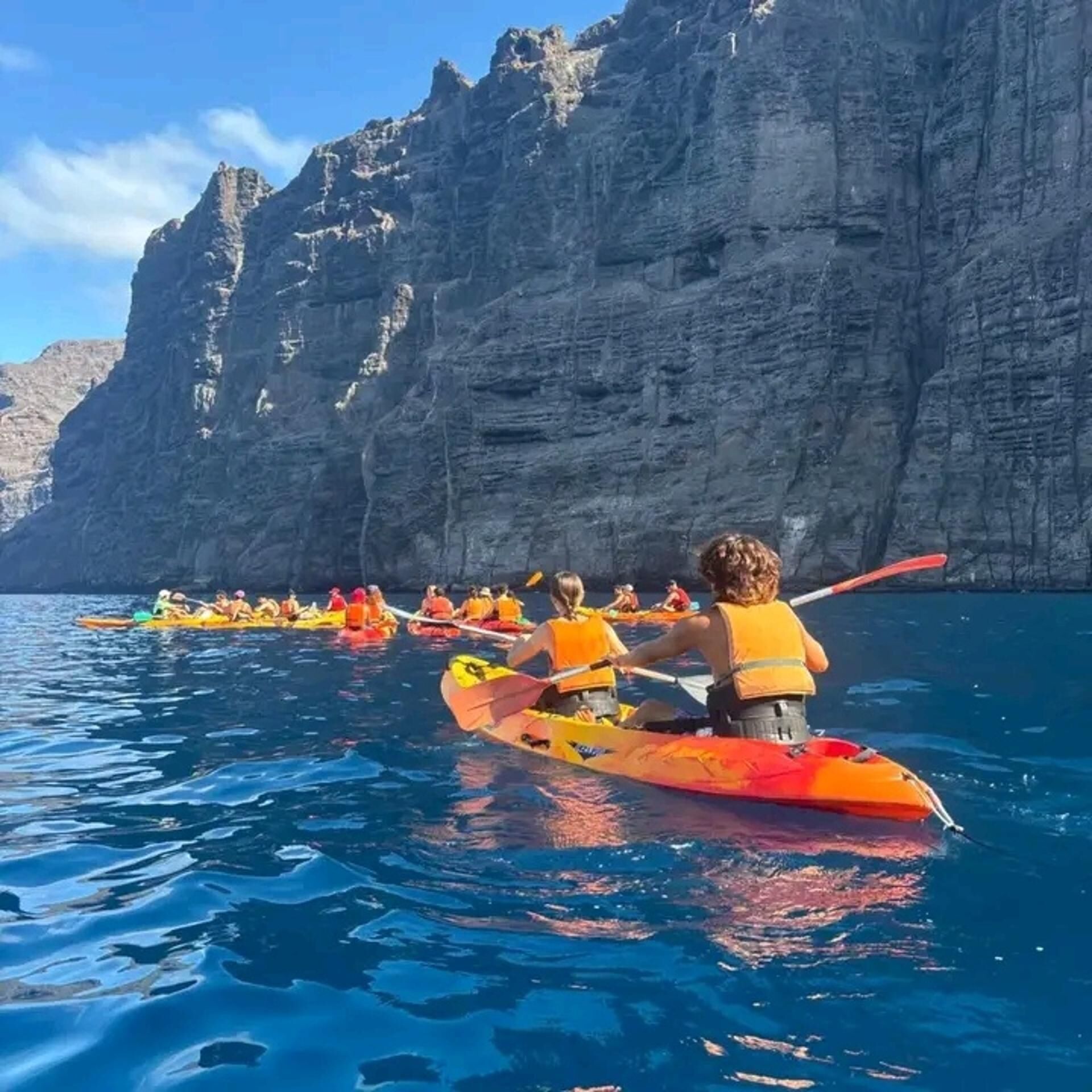 Un groupe de personnes pratiquant le kayak sur une étendue d’eau, avec des falaises rocheuses en arrière-plan.
