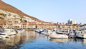 Marina com barcos atracados, encosta com edifícios e céu claro.