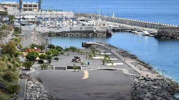 A coastal marina with boats, a rocky shoreline, and a paved walkway.