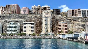 A coastal cityscape with high-rise buildings, rocky cliffs, and a clear blue sea.