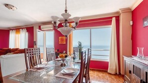 A dining area with a table set for four, a chandelier, and a view of the sea.