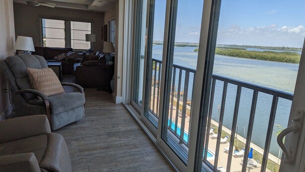 Ein geräumiger Balkon mit Blick auf ruhiges Gewässer, eine Sitzecke mit Sofa und Sesseln sowie ein kleiner Poolbereich.