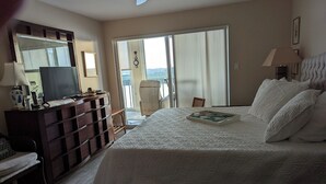 Ein Schlafzimmer mit einem großen Bett, einem Schminktisch, einem Fernseher und Blick ins Freie durch eine Schiebetür.