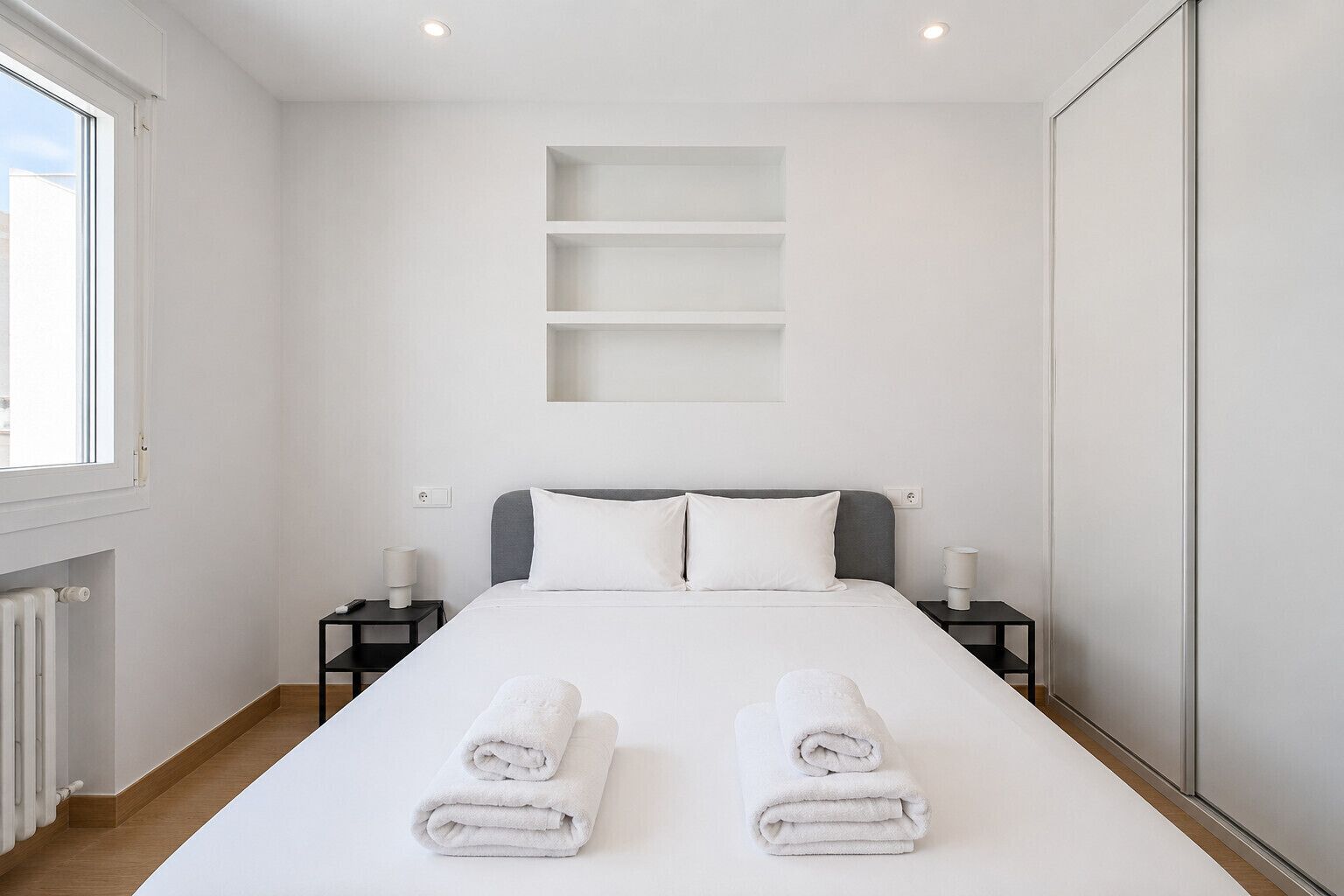 Une chambre d’hôtel avec un lit, deux tables de chevet, un radiateur et une fenêtre.