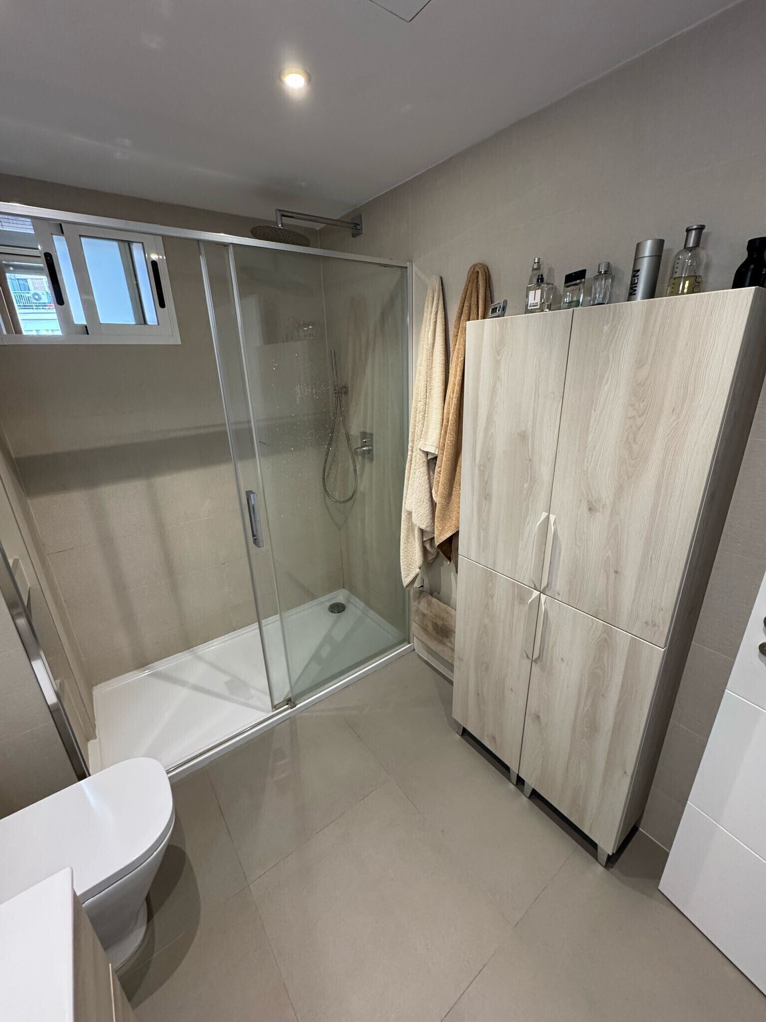 A modern bathroom with a glass-enclosed shower, a toilet, and a wooden wardrobe.
