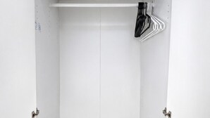 Un armario blanco con espejo plano, barra para colgar y suelo de madera.