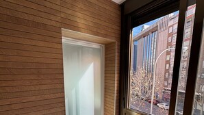 Un interior moderno con paneles de madera, un puerta corredera de vidrio que da a un balcón y vistas a un paisaje urbano.