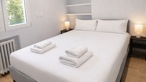Un dormitorio moderno con una cama grande, dos lámparas de noche, un radiador y una ventana con persianas.