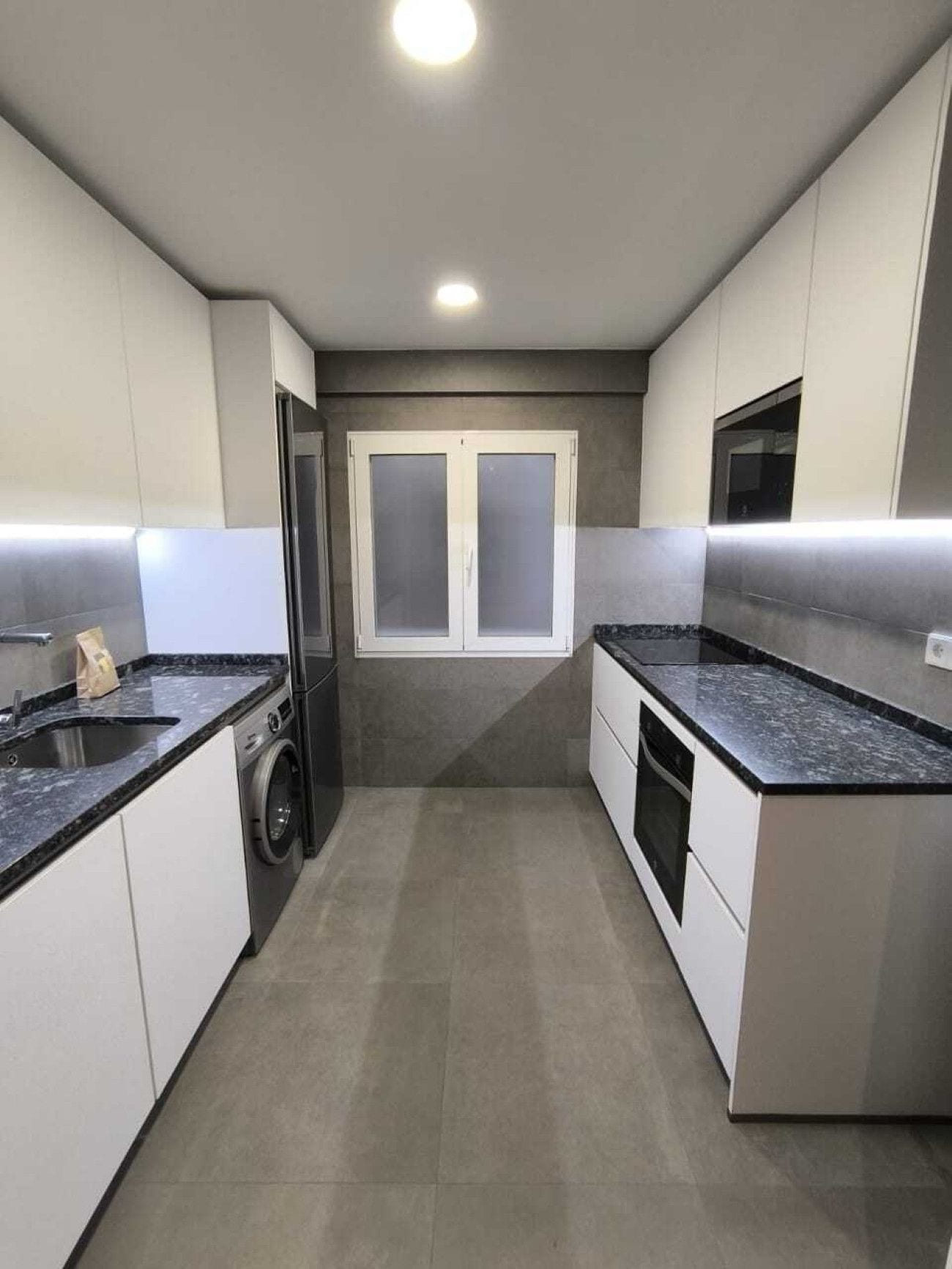 Een moderne keuken met een wasmachine, een magnetron en een groot raam met dubbel glas.