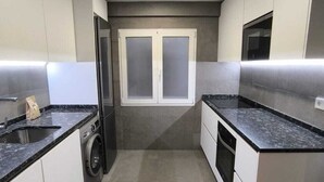A modern kitchen with a washing machine, a microwave, and a double door window.
