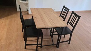 A rectangular wooden table with four black chairs, a white wall, and a wooden floor.