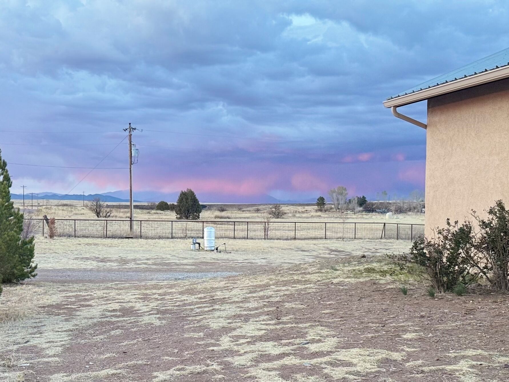 Paisaje rural con un cercado, un edificio y una línea eléctrica.