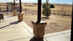 Un patio cubierto con pilares de piedra, vistas a un paisaje seco y una zona amurallada.