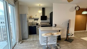 A modern kitchen with a dining area, a refrigerator, a sink, and a coffee maker.