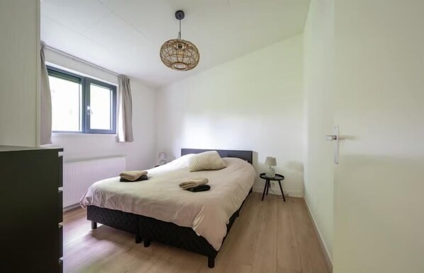 A bedroom with a bed, bedside table, lamp, and a hanging light fixture.