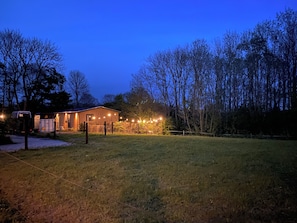Surrounded by tall trees, this serene outdoor space features a grassy area, a wooden fence, and a cozy building with a sloped roof.