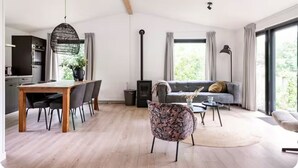 A modern living room with a sofa, a dining table with chairs, a fireplace, and large windows. - Luxury holiday cottage, stunning views, and hot tub. (Pingjum)