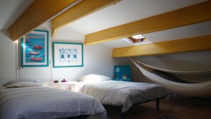 Een slaapkamer met twee bedden, een hangmat, houten balken en kunstwerken aan de muur.