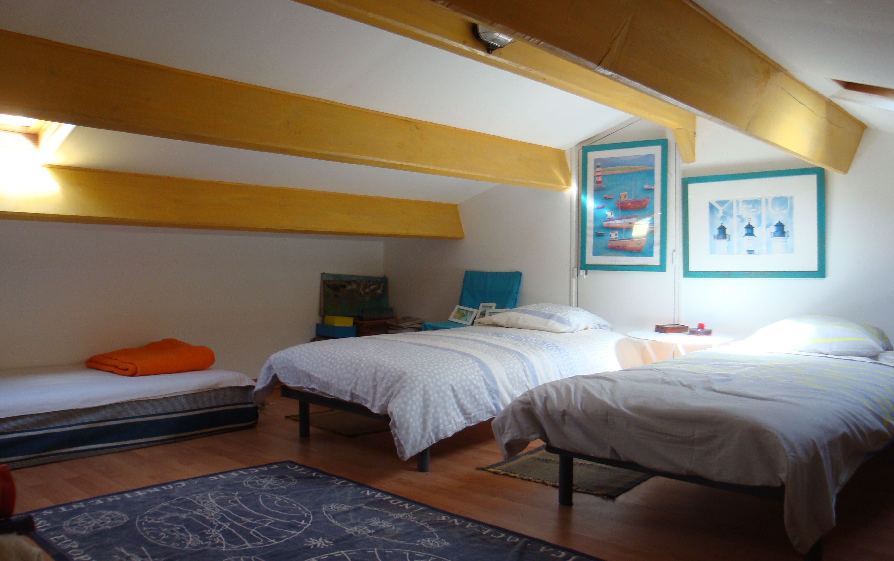 A bedroom with two beds, a wooden ceiling, and artwork on the walls.