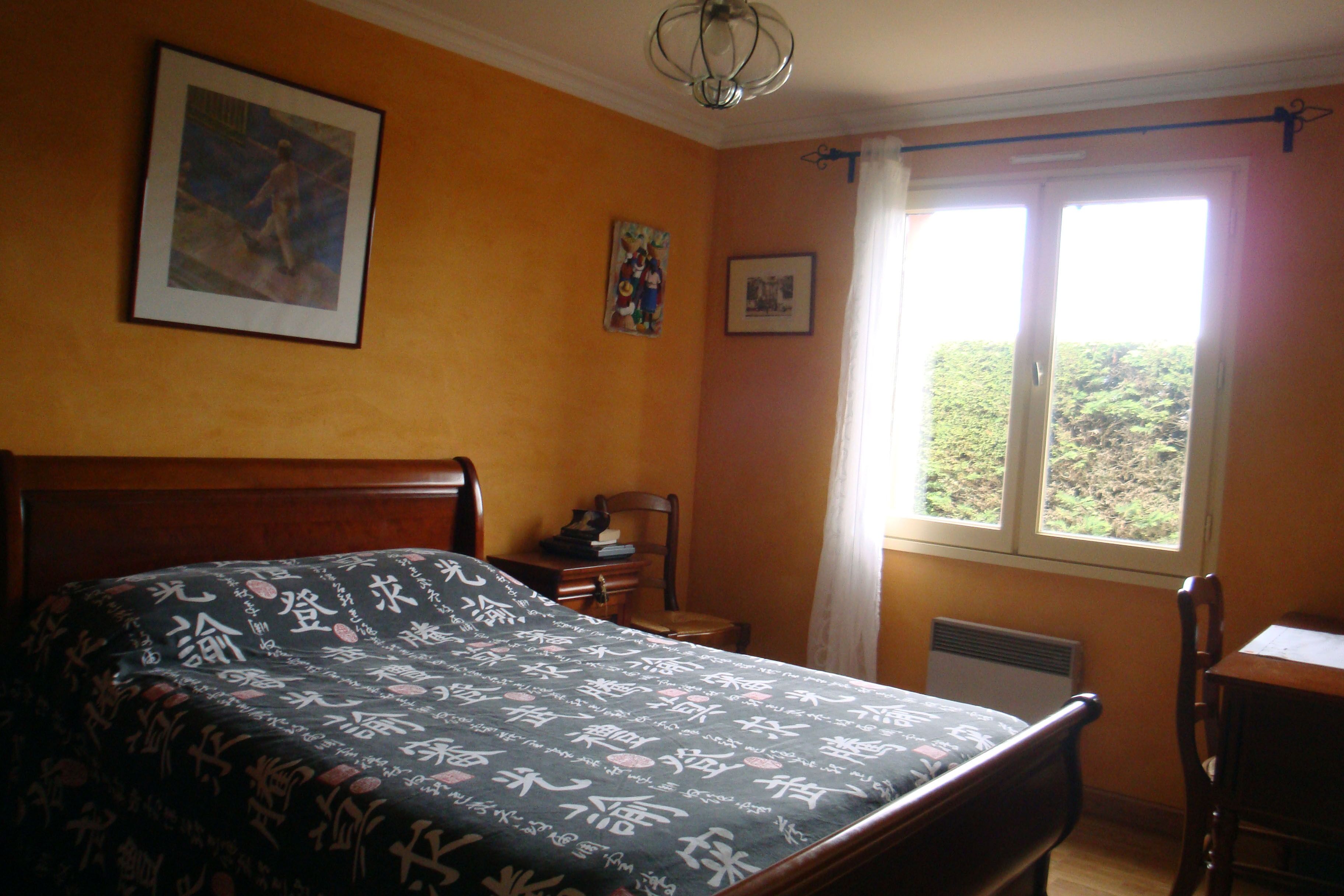 Ein Schlafzimmer mit Bett, Stuhl, Schreibtisch und einem Fenster mit Blick auf Grünflächen.