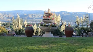 A tiered garden fountain with flowers, surrounded by potted plants and a view of mountains.