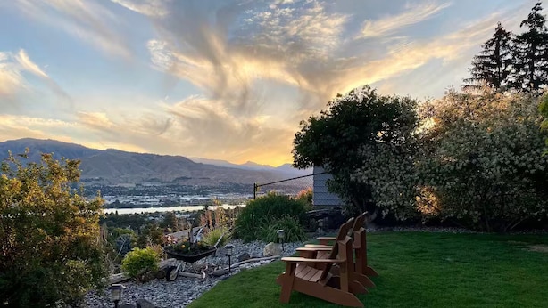 A grassy outdoor area with a wooden bench, a stone pathway, and a view of a valley and mountains in the distance.