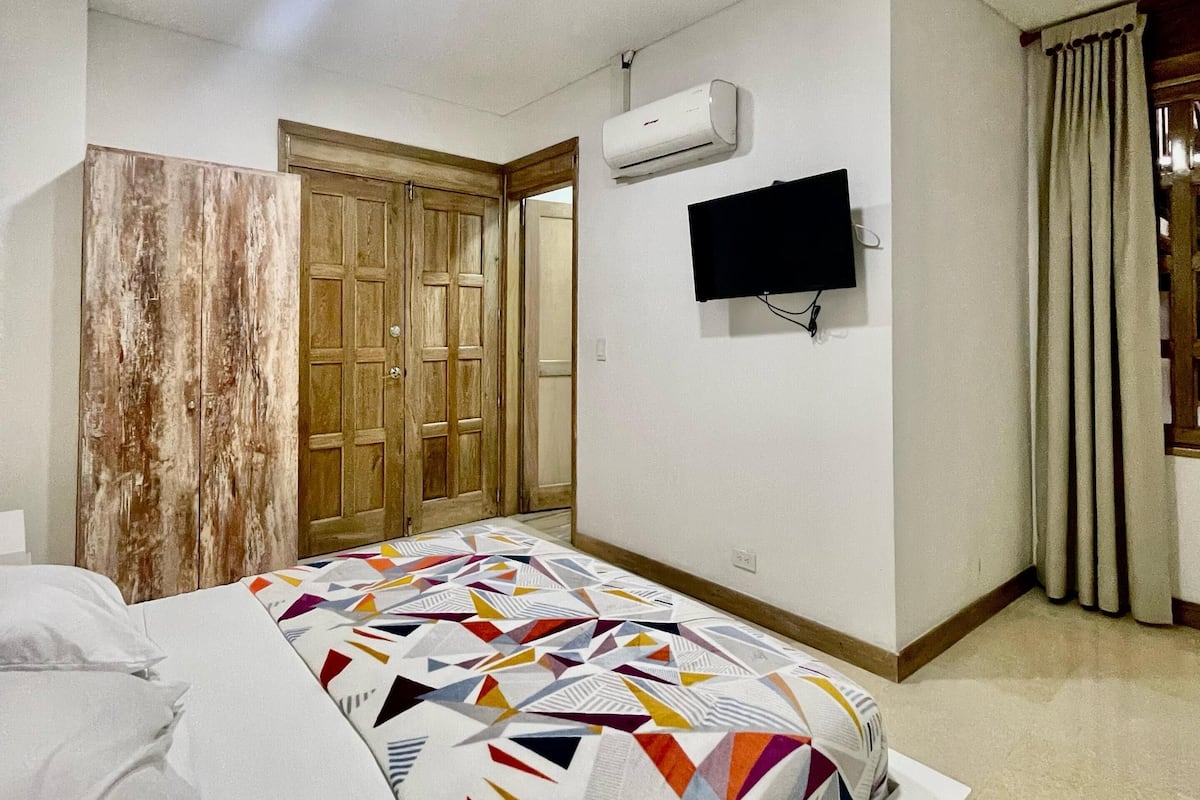 A bedroom with a bed, a TV, an air conditioning unit, and a wooden wardrobe.