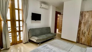 Quarto com cama, sofá, televisão e ar condicionado.