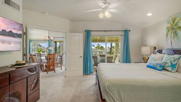 A bedroom with a bed, a dresser, a ceiling fan, a TV, and a view of the outdoors.