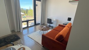 A modern living room with a large sliding glass door leading to an outdoor area, a sofa, a small table with a vase, and a desk with a chair. - Modern Private Casita • Bright, Quiet, Minutes to LANL & Trails (Los Alamos)