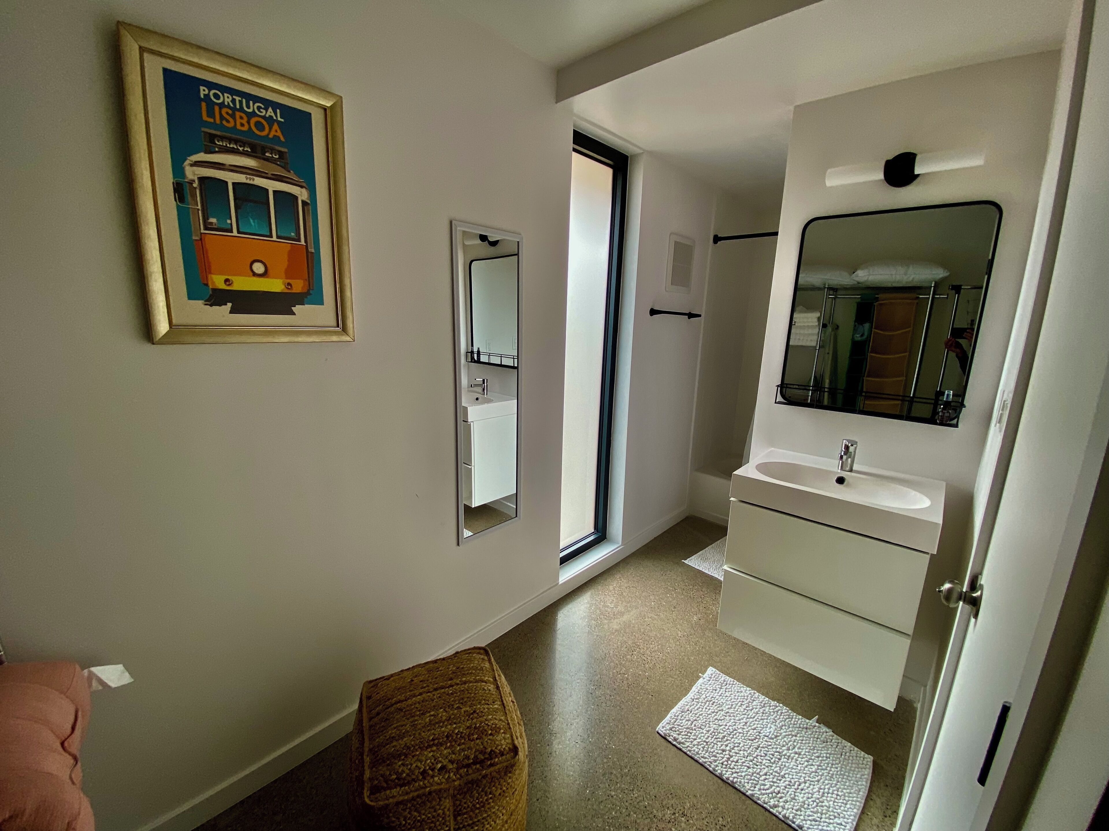 Een moderne badkamer met een witte wastafel, spiegel en een afbeelding van een tram in een lijst.