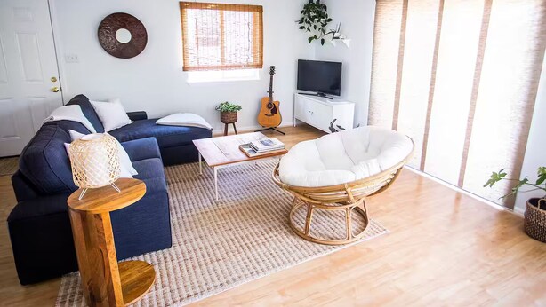 Ein Wohnzimmer mit einem dunkelblauen Sofa, einem weißen Sessel, einem Holztisch und einer TV-Konsole mit einer Gitarre.
