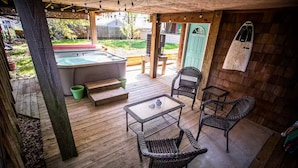 Eine überdachte Terrasse im Freien mit Whirlpool, Korbstühlen und einem Tisch.