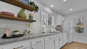 Una cocina moderna con armarios blancos, una encimera de mármol y un estante de madera.