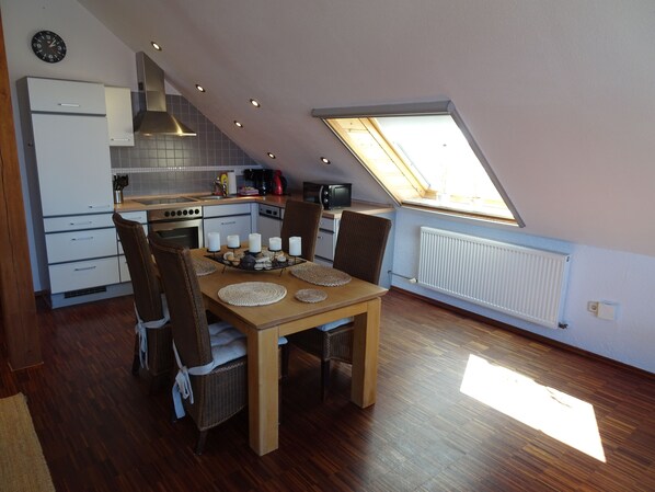 A modern kitchen with a dining area, featuring a skylight, wooden flooring, and a clock on the wall.