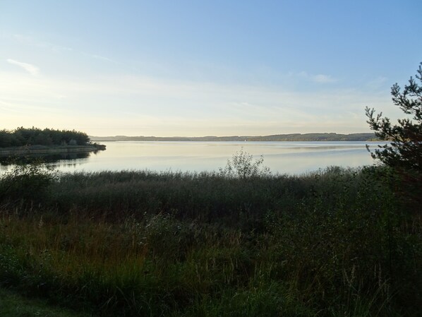 A calm lake with a forested shoreline and distant hills.