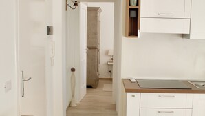 A modern, minimalist living room with a beige sofa and a wooden coffee table. A kitchen area is visible with white cabinetry and a wooden countertop. - New two-room apartment with residential pool, large terrace and exclusive parking space (Bordighera)