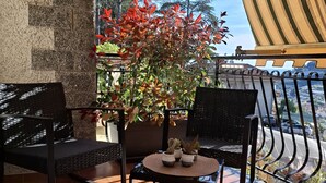 A patio with two black wicker chairs, a small round table, and a potted plant with red leaves. - New two-room apartment with residential pool, large terrace and exclusive parking space (Bordighera)