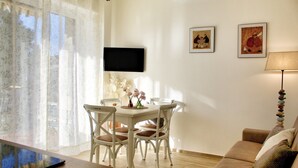 A dining area with a table and chairs, a flat-screen TV mounted on the wall, and a sofa. - New two-room apartment with residential pool, large terrace and exclusive parking space (Bordighera)