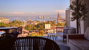 Un balcón con vistas a un paisaje urbano, incluyendo una torre destacada, y una zona de estar con sofá y sillas.